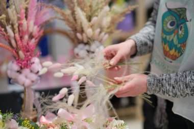 Dükkan sahibi, yerel bir zanaatkar pazarında elinde bir buket kurumuş çiçekle tezgahın arkasında satış yapıyor. Küçük bir iş. Genç bayan girişimci çiçek bayramı kompozisyonu satıyor..