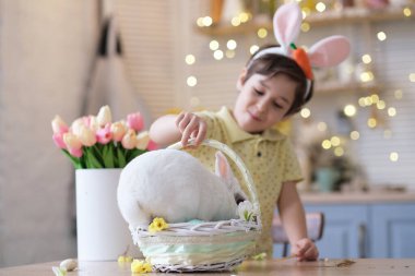 Mutlu Paskalyalar. Tavşan kulaklı ve tavşanlı çocuk bahar tatili kutlaması için sepette oturuyor. Tavşana odaklan, dikkatini dağıt..