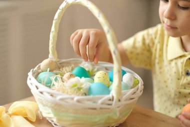 Tavşan kulaklı çocuk masada mutfakta oturuyordu. Paskalya için hazırlanan boyalı yumurtaları tutan çocuk.