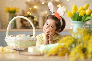 Tavşan kulaklı çocuk masada mutfakta oturuyordu. Paskalya için hazırlanan boyalı yumurtayı tutan sevimli bir çocuğun portresi..