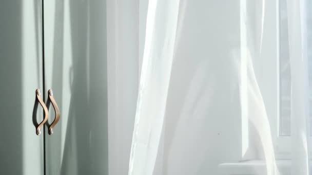 Soleil du matin brillant dans la fenêtre ouverte à travers les rideaux. Rideau d'agitation blanc abstrait dans un appartement de chambre à coucher blanche. — Video