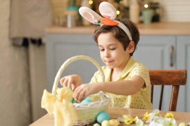 Tavşan kulaklı çocuk masada mutfakta oturuyordu. Paskalya için hazırlanan boyalı yumurtaları tutan çocuk.