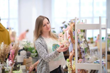 Dükkan sahibi, yerel bir zanaatkar pazarında elinde bir buket kurumuş çiçekle tezgahın arkasında satış yapıyor. Küçük bir iş. Genç bayan girişimci çiçek bayramı kompozisyonu satıyor..