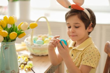 Tavşan kulaklı çocuk masada mutfakta oturuyordu. Paskalya için hazırlanan boyalı yumurtaları tutan çocuk.