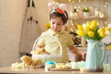 Paskalya yumurtası ve tavşan kulaklı neşeli çocuk mutfakta oynuyor. Mutlu çocuk Paskalya için hazırlanıyor.