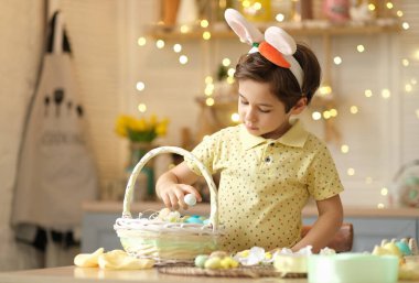 Tavşan kulaklı çocuk masada mutfakta oturuyordu. Paskalya için hazırlanan boyalı yumurtaları tutan çocuk.