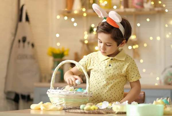Tavşan kulaklı çocuk masada mutfakta oturuyordu. Paskalya için hazırlanan boyalı yumurtaları tutan çocuk.