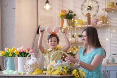 Paskalya ailesi eğlencesi. Tavşan kulaklı çocuklar ve annem mutfakta tatil için masayı dekore ediyorlar.