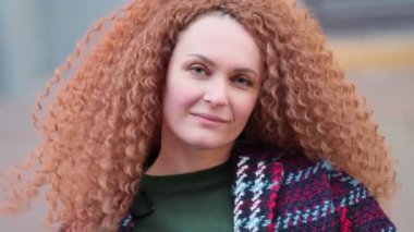 Güzel genç bir kadın kameraya bakıyor ve neşeyle gülümsüyor. Gün ışığında sokakta gülen surat. Dışarıda olumlu bir portre var. Kapatın. Yavaş çekim videosu. depolama görüntüleri