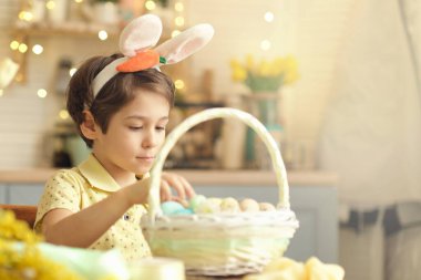 Tavşan kulaklı çocuk masada mutfakta oturuyordu. Paskalya için hazırlanan boyalı yumurtaları tutan çocuk.