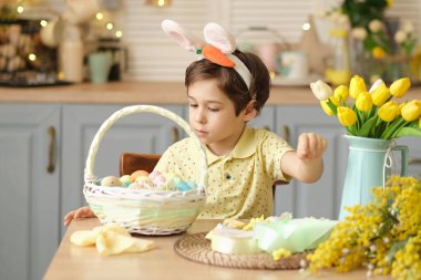 Tavşan kulaklı çocuk masada mutfakta oturuyordu. Paskalya için hazırlanan boyalı yumurtaları tutan çocuk.