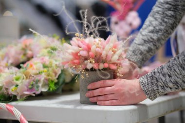 Dükkan sahibi, yerel bir zanaatkar pazarında elinde bir buket kurumuş çiçekle tezgahın arkasında satış yapıyor. Küçük bir iş. Genç bayan girişimci çiçek bayramı kompozisyonu satıyor..