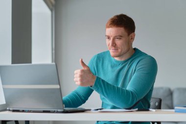 Adam evinde, masasında gülümseyen bir dizüstü bilgisayar kullanıyor ve video iletişimiyle meslektaşına bir benzerlik gösteriyor..