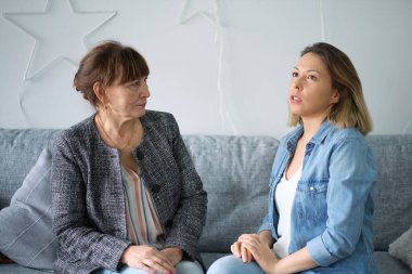 Yetişkin kızı yaşlı annesiyle konuşuyor. Anne ve kızı sohbetten zevk alıyorlar modern oturma odasındaki koltukta oturuyorlar. veli ilişkisi kavramı