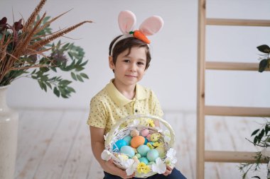 Tavşan kulağı takan çocuk. Yerde oturan ve elinde bir sepet dolusu şekerlemeyle bir çocuğun portresi. Paskalya yumurtası avında eğleniyoruz..