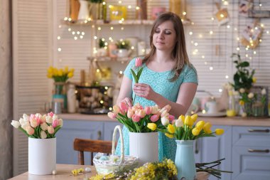 Kadın evini çiçeklerle süslüyor. Kadın mutfakta bir buket lale topluyor. bahar havası