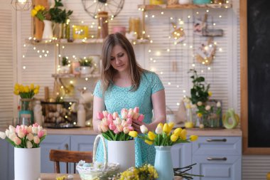 Kadın evini çiçeklerle süslüyor. Kadın mutfakta bir buket lale topluyor. bahar havası
