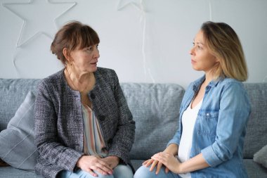 Yetişkin kızı yaşlı annesiyle konuşuyor. Anne ve kızı sohbetten zevk alıyorlar modern oturma odasındaki koltukta oturuyorlar. veli ilişkisi kavramı
