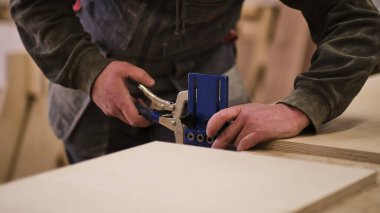 Kapatın. Marangoz çalışma bankında bir mezura tutuyor. Ahşap işleri ve mobilya yapma konsepti. Atölyedeki marangoz mobilya dolabının parçalarını işaretleyip monte ediyor.