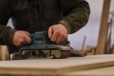 Kapatın. Atölyedeki marangoz elektrikli çim biçme makinesi ile ahşap tahtayı parlatıyor. Ahşap işleri ve mobilya yapma kavramı.