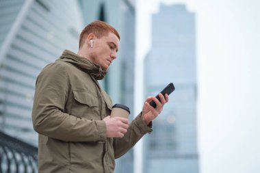 Siyah takım elbiseli genç başarılı iş adamı modern ofis gökdeleninde çalışırken akıllı telefon kullanıyor.