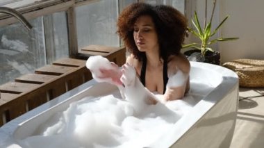 Gülümseyen ve rahatlatan Afro-Amerikan kadın köpük dolu bir küvette banyo yapıyor. Harika bir zaman. Yaşam tarzı insan kavramı