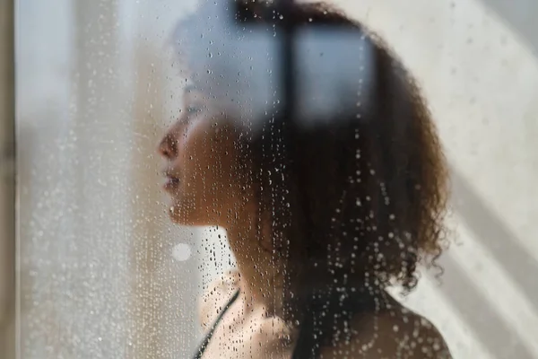 Smyslný portrét mladé ženy, jak se sprchuje. Rozostřená žena se dívá přes sklo sprchového koutu. — Stock fotografie