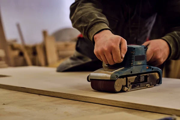 De cerca. Carpintero en taller pule tablero de madera con una lijadora orbital eléctrica. Concepto de carpintería y mobiliario. —  Fotos de Stock