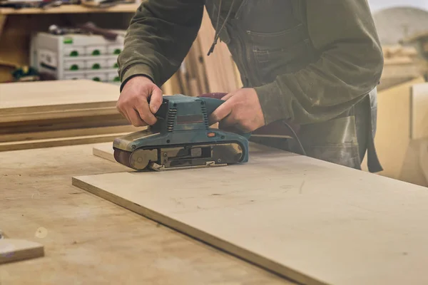 Kapatın. Atölyedeki marangoz elektrikli çim biçme makinesi ile ahşap tahtayı parlatıyor. Ahşap işleri ve mobilya yapma kavramı. — Stok fotoğraf