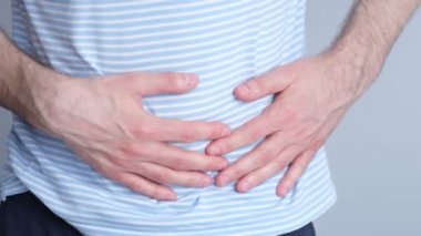 Mide ağrısı çeken bir adam. Karın ağrısı sorunu olan bir adam ishal, gri arka plan, insanlar, sağlık ve problem konsepti. Yavaş çekim, yumuşak odaklanma