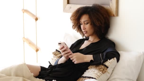 Νεαρή όμορφη Αφροαμερικανή γυναίκα γραπτών μηνυμάτων σε smartphone ή βλέποντας κοινωνικό δίκτυο — Αρχείο Βίντεο