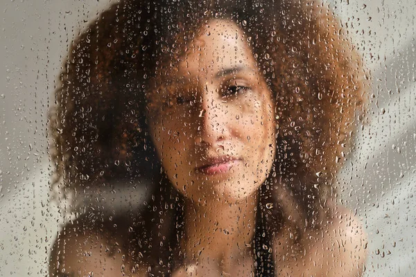 Чувственный портрет молодой женщины, принимающей душ. Расслабленная женщина смотрит через стекло душевой кабинки. Арт-портрет. Женская красота. Skincare wellness. — стоковое фото