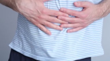 Mide ağrısı çeken bir adam. Karın ağrısı sorunu olan bir adam ishal, gri arka plan, insanlar, sağlık ve problem konsepti. Yavaş çekim, yumuşak odaklanma