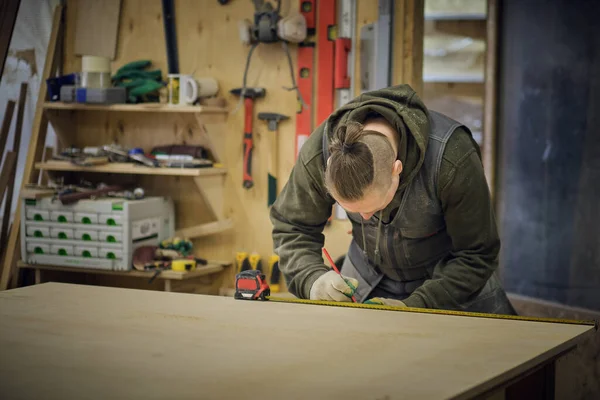 Charpentier tenant une bande de mesure sur le banc de travail. Concept de menuiserie et de fabrication de meubles. Menuisier dans l'atelier marque et assemble des parties de l'armoire à meubles — Photo