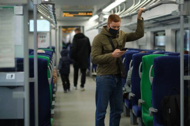 Solunum cihazındaki yakışıklı adam akıllı telefon kullanıyor ve metroda ya da trende gidip gelirken kalabalığa mesafeli davranıyor. Enfeksiyon ve hava kirliliğini önleme kavramı