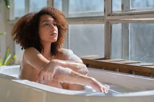 Sorrindo e relaxando afro-americana tomando banho em uma banheira cheia de espuma. Um tempo incrível. conceito de pessoas estilo de vida — Fotografia de Stock