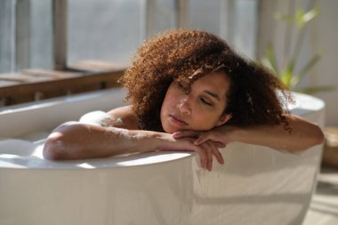 Gülümseyen ve rahatlatan Afro-Amerikan kadın köpük dolu bir küvette banyo yapıyor. Harika bir zaman. Yaşam tarzı insan kavramı