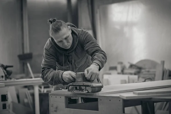 Ferme là. Menuisier à l'atelier polit la planche en bois avec une ponceuse orbitale électrique. Concept de menuiserie et de fabrication de meubles. photographie noir et blanc — Photo