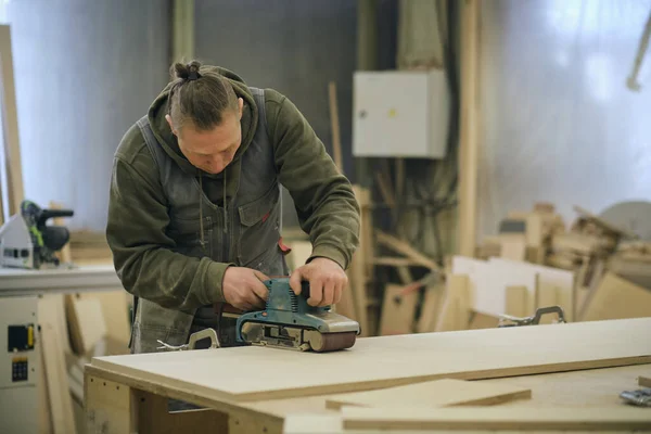 Aus nächster Nähe. Tischler in der Werkstatt poliert Holzbretter mit einem Elektroschleifer. Konzept der Holz- und Möbelherstellung. — Stockfoto