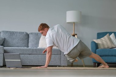 Genç aktif adam dizüstü bilgisayarda video eğitimi izliyor, egzersiz yapıyor, sabah evde egzersiz yapıyor. Spor, sağlıklı yaşam tarzı. Evde Forma gir.