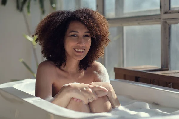 微笑和放松的非洲裔美国女人沐浴在充满泡沫的浴缸里。令人惊奇的时刻生活方式概念 — 图库照片
