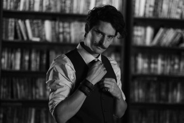 Karanlık bir kütüphane odasında düşünceli bir adam gece ayakta duruyor. Bıyıklı şık bir adam bileziği düzeltiyor. siyah ve beyaz fotoğrafçılık