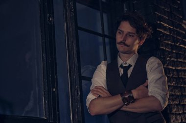 Şık giyinmiş bir adam pencerede durur ve mesafeye bakar. Düşünceli adam gece karanlık bir odada duruyor.