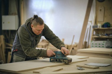 Kapatın. Atölyedeki marangoz elektrikli çim biçme makinesi ile ahşap tahtayı parlatıyor. Ahşap işleri ve mobilya yapma kavramı.