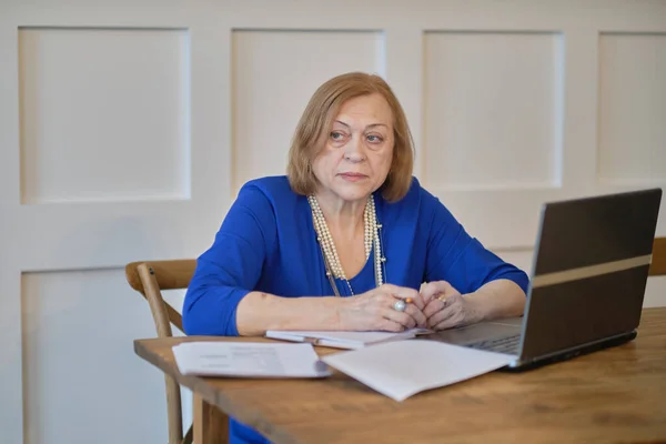 Mujer mayor que utiliza el ordenador portátil para navegar por Internet en su cocina. El concepto de empleo de alto nivel, seguridad social. Señora madura sentada en el trabajo escribiendo una computadora portátil en una oficina en casa. —  Fotos de Stock