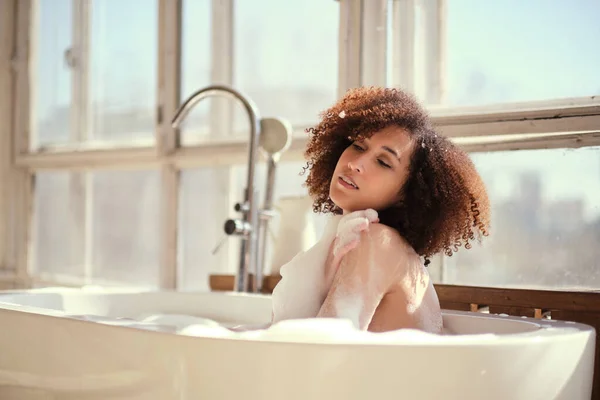 Gülümseyen ve rahatlatan Afro-Amerikan kadın köpük dolu bir küvette banyo yapıyor. Harika bir zaman. Yaşam tarzı insan kavramı — Stok fotoğraf