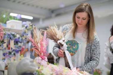 Dükkan sahibi, yerel bir zanaatkar pazarında elinde bir buket kurumuş çiçekle tezgahın arkasında satış yapıyor. Küçük bir iş. Genç bayan girişimci çiçek bayramı kompozisyonu satıyor..