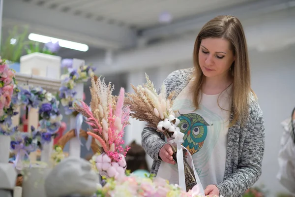 business owner selling behind counter with her bouquet of dried flowers at local market of craftsmen, small business. young woman entrepreneur sells floral holiday composition.