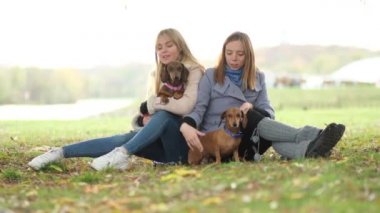Ağır çekim. Parkta iki kız arkadaş köpekleriyle oynuyorlar. kız kardeş ilişkisi. Parkta oynayıp eğlenerek bir gün geçir. Görüntüyü kapat.