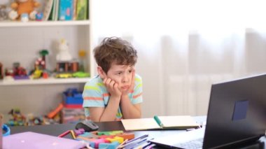 Üzgün çocuk ödevlerini yaparken dizüstü bilgisayarın önünde oturuyor. Çevrimiçi öğrenme güçlüğü konsepti, okul çocuğu stres altında. Yumuşak odaklanma, çözülme